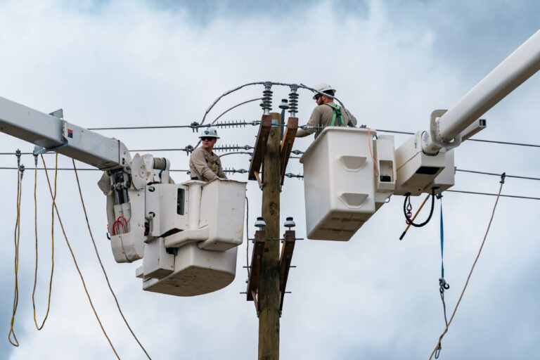 Two Santee Cooper lineworkers in a bucket truck working on electrical equipment. 