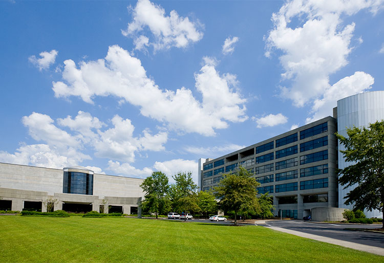 Office building in front of a blue sky and white clouds and green grass.